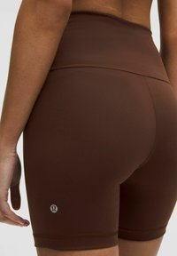 Hnedé šortky s vysokým pásom vyrobené z hladkej, pružnej tkaniny. Majú priliehavý strih a decentné logo blízko lemu. Mäkka textúra, bezšvové dokončenie.