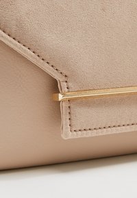 Clutch in suede e pelle beige con un accento in metallo dorato. Presenta linee pulite, cuciture visibili e una superficie testurizzata.