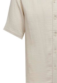 Short-sleeve, button-up shirt in light beige, made of textured, quilted fabric with a grid pattern and soft, smooth finish.