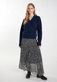 Mörkblå kabelstickad tröja med omslagdesign och sidoknappar, kombinerad med en flödande maxikjol i svart och vitt mönster samt svarta ankelstövlar.
