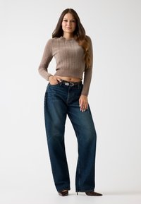 Brauner, gestrickter, kürzerer Pullover mit strukturiertem Muster, kombiniert mit weit geschnittenen, dunklen Denim-Jeans und schwarzen, spitzen High Heels.