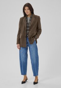 Blazer din suede maro cu revere tăiate, două buzunare frontale, purtat peste o cămașă cu carouri, asortat cu blugi cu talie înaltă și pantofi negri cu toc.