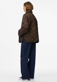Bruine gewatteerde jas met een hoge kraag, verlaagde schouders en een rechte snit, gecombineerd met donkerblauwe wijde jeans en witte sneakers.