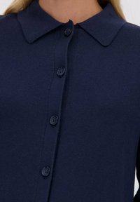 Marineblauwe gebreide cardigan met een puntige kraag, zes knoopsluitingen en een soepele textuur. Casual ontwerp, geschikt voor layering.