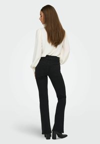 Vaqueros acampanados negros de mezclilla, con cintura alta, bolsillos traseros y combinados con una blusa de textura clara.