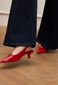 Décolleté in vernice rossa con punta affusolata e tacco a blocco piccolo, abbinati a pantaloni larghi in denim scuro.