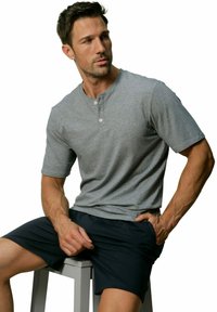 Grijze henley shirt met korte mouwen, met een drie-knopen knoopsluiting. Gecombineerd met donkere shorts, zittende pose tegen een witte achtergrond.