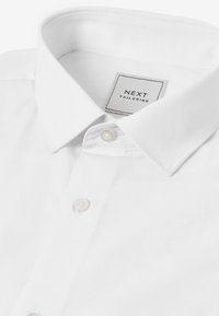 Bela po meri krojena srajca z vrtastim ovratnikom in belimi gumbi, na notranji strani ovratnika je etiketa znamke "NEXT TAILORING".