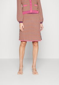 Ensemble robe tricotée et cardigan avec un motif géométrique rose et orange, des poignets côtelés et un ourlet carré, associé à des sandales transparentes.