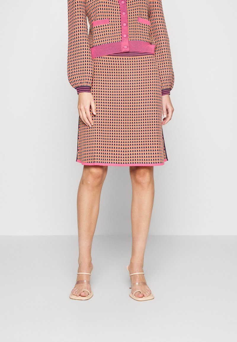 Ensemble robe tricotée et cardigan avec un motif géométrique rose et orange, des poignets côtelés et un ourlet carré, associé à des sandales transparentes.