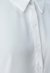 White button-up shirt featuring a classic collar, smooth fabric, and six buttons along the front, highlighting a clean and minimal design.
