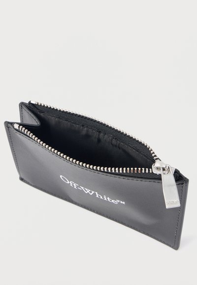 Μαύρο δερμάτινο πορτοφόλι κάρτας Off-White με φερμουάρ, ανοιχτό που δείχνει μία θήκη με ασημί φερμουάρ και χαρακτηριστικό τράβηγμα με το λογότυπο, σε λευκό φόντο.