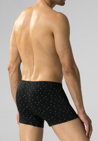 Czarne bokserki z zielonym wzorem liści, wykonane z gładkiego materiału z elastycznym pasem. Widoczne detale szycia.