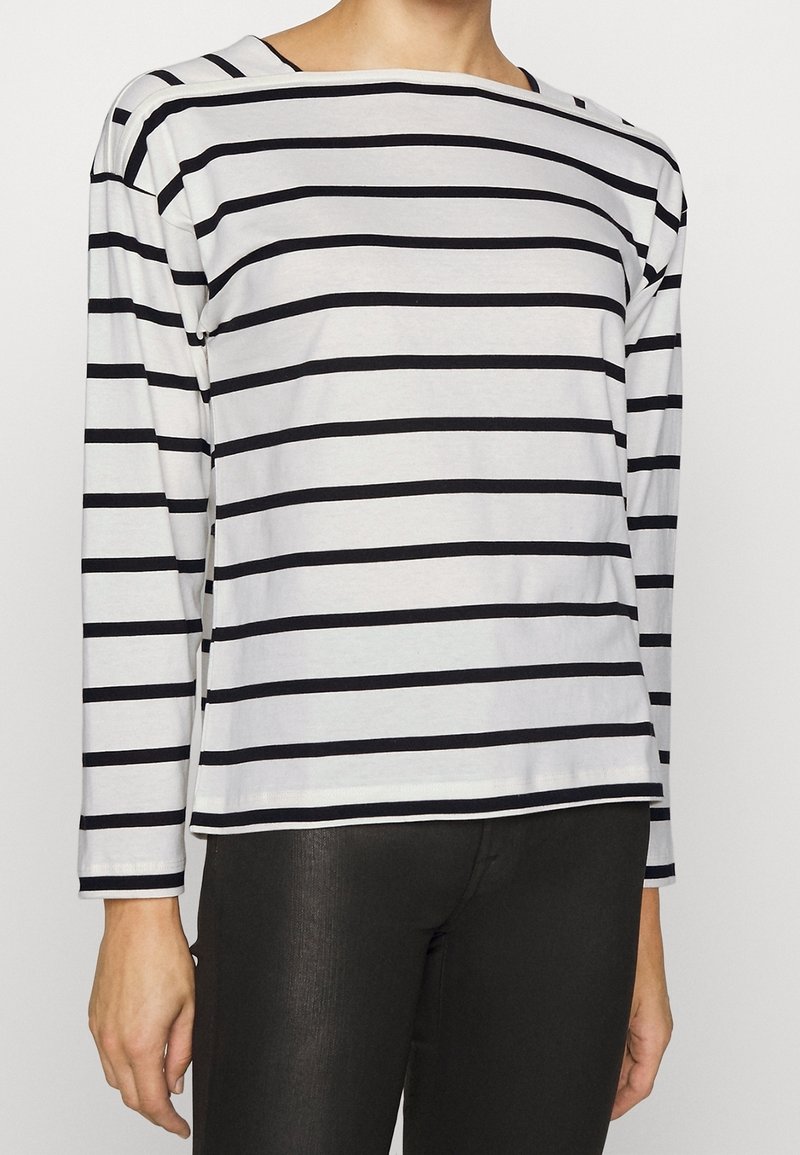 Long-sleeve striped shirt in white with black horizontal stripes, featuring a boat neckline and soft fabric. Black fitted pants worn underneath.