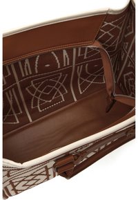 Interno di borsa tote in pelle marrone e tessuto con motivi geometrici, una tasca con cerniera e rifinitura beige chiaro lungo il bordo superiore.