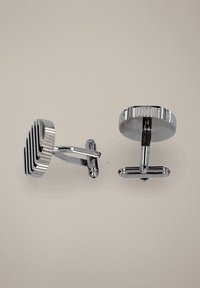 Srebrne spinki do mankietów o okrągłym kształcie, z teksturowanym paskowanym wzorem z jednej strony i gładkim wykończeniem z drugiej. Wykonane z metalu.