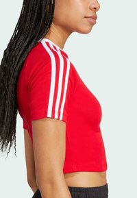 Red short-sleeve crop top made of cotton, featuring three white stripes on each shoulder and a fitted design.