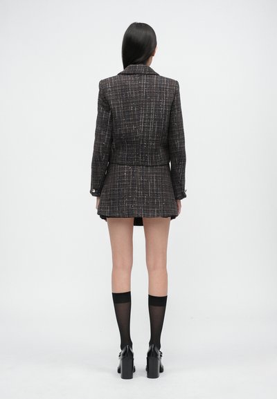 Mustast ja pruunist ruuduline bleiser koos sobiva seelikuga, kohandatud lõige, tekstuuriga kangas. Mustad põlvikud ja paksud kontsaga kingad viimistlevad välimuse.