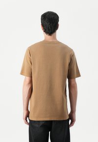 Camiseta de algodón marrón con mangas cortas, cuello redondo y un corte estándar. Presenta un diseño liso sin patrones ni adornos.