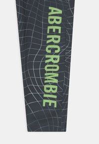 Czarne legginsy z wzorem kratki w odcieniach szarości z jaskrawozielonym napisem "ABERCROMBIE" na jednym boku. Gładki, elastyczny materiał, dopasowany krój.