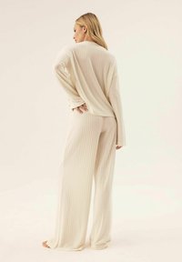 Cream ribbed long-sleeve top and wide-leg pants set, featuring a relaxed fit and soft texture, with a subtle vertical stripe pattern.