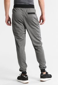 Graue Jogginghosen mit einem gerafften Bund, elastischen Bündchen und einer kleinen Gesäßtasche mit einem schwarzen Akzent. Getragen mit schwarzen Sportschuhen.