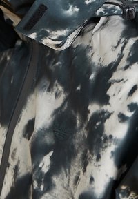 Kurtka w czarno-białe chmurki o matowym wykończeniu. Posiada subtelne logo oraz zapięcie na rzep przy kołnierzu. Trwała tekstura materiału.