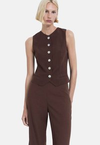 Bruine mouwloze top met een aansluitend ontwerp, voorzien van een ronde halslijn, zes lichte knopen aan de voorkant en een peplum-stijl zoom.