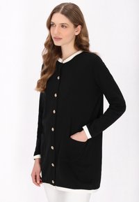Cardigan lung negru cu guler și manșete albe, av�ând detalii cu nasturi aurii și buzunare laterale. Material neted cu o croială lejeră.