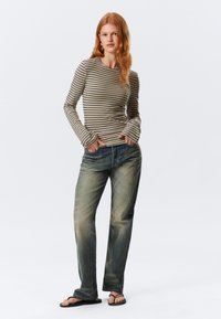 Gestreepte lange mouw top in beige en olijfgroen, relaxte pasvorm; blauwe rechte spijkerbroek; zwarte teenslippers; soepele stof, subtiele texturen.