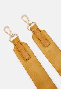 Keltaiset kangashihnat, joissa on teksturoidut ruskeat nahkakoristeet. Kullatut metallikoukut kummassakin päässä. Yksinkertainen ja toimiva muotoilu.