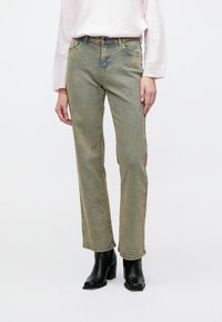 Svetlo zelené džínsy z denimu so strihom na rovno, jemným vrásnením a miernym bledením. Kombinované s čiernymi členkovými čižmami na podpätku.