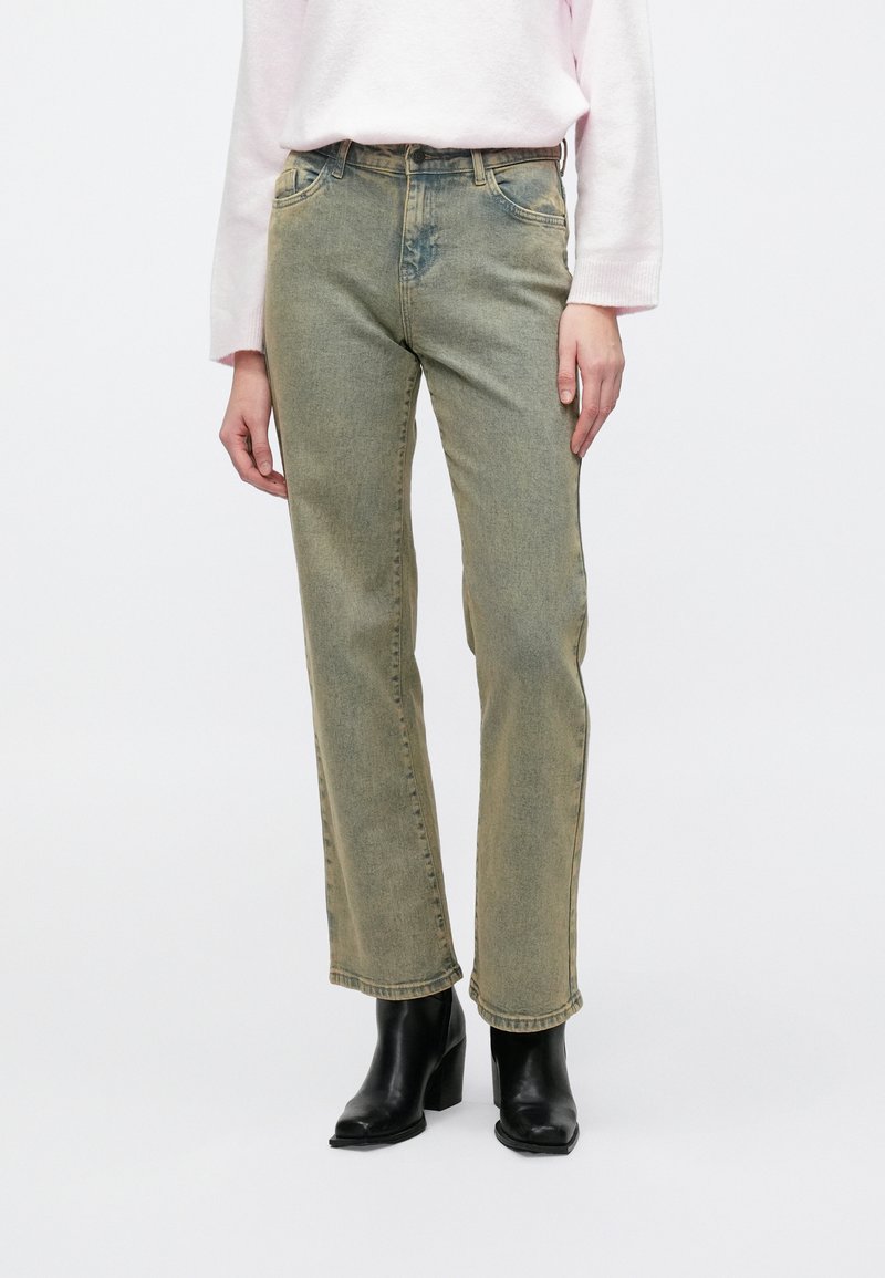 Svetlo zelené džínsy z denimu so strihom na rovno, jemným vrásnením a miernym bledením. Kombinované s čiernymi členkovými čižmami na podpätku.