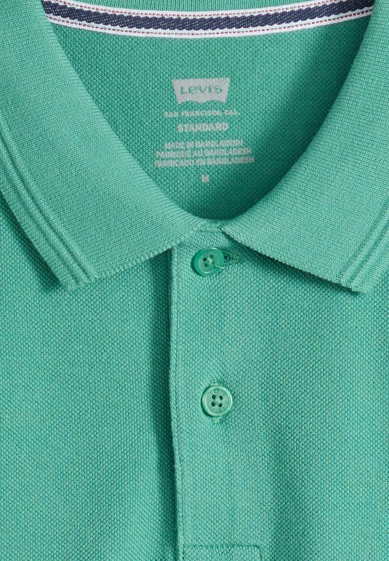 Polo verde texturizado con dos botones abrochados y un cuello acanalado que presenta un ribete a rayas en el interior.