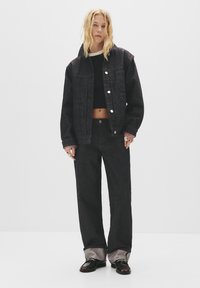 Zwarte spijkerjas en wijde jeans, met een cropped zwart topje eronder, voorzien van zilveren knopen, een relaxte pasvorm en contrasterende manchetten.