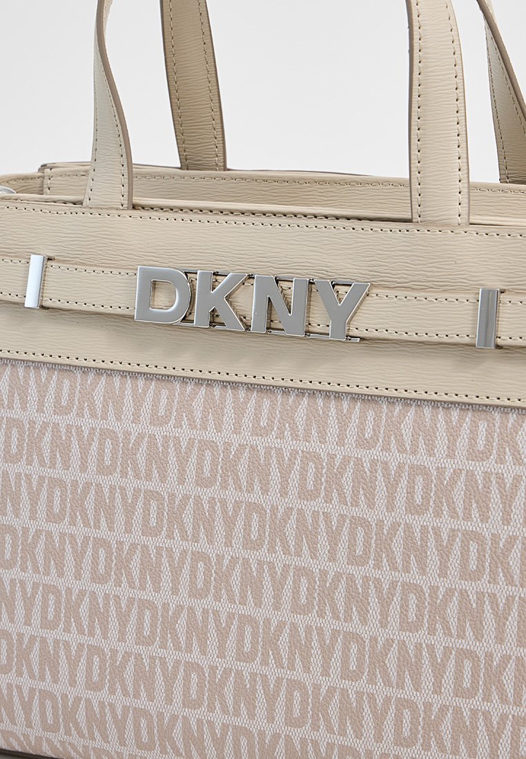 Beige Tote-Bag mit DKNY-Logo, strukturiertem Material und wiederholendem Markenmuster, ausgestattet mit silberner Hardware und doppelten Obergriffen.