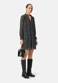 Vestido negro con lunares, con un escote con volantes, llevado con botas de cuero negras hasta la rodilla con hebillas y un pequeño bolso negro.