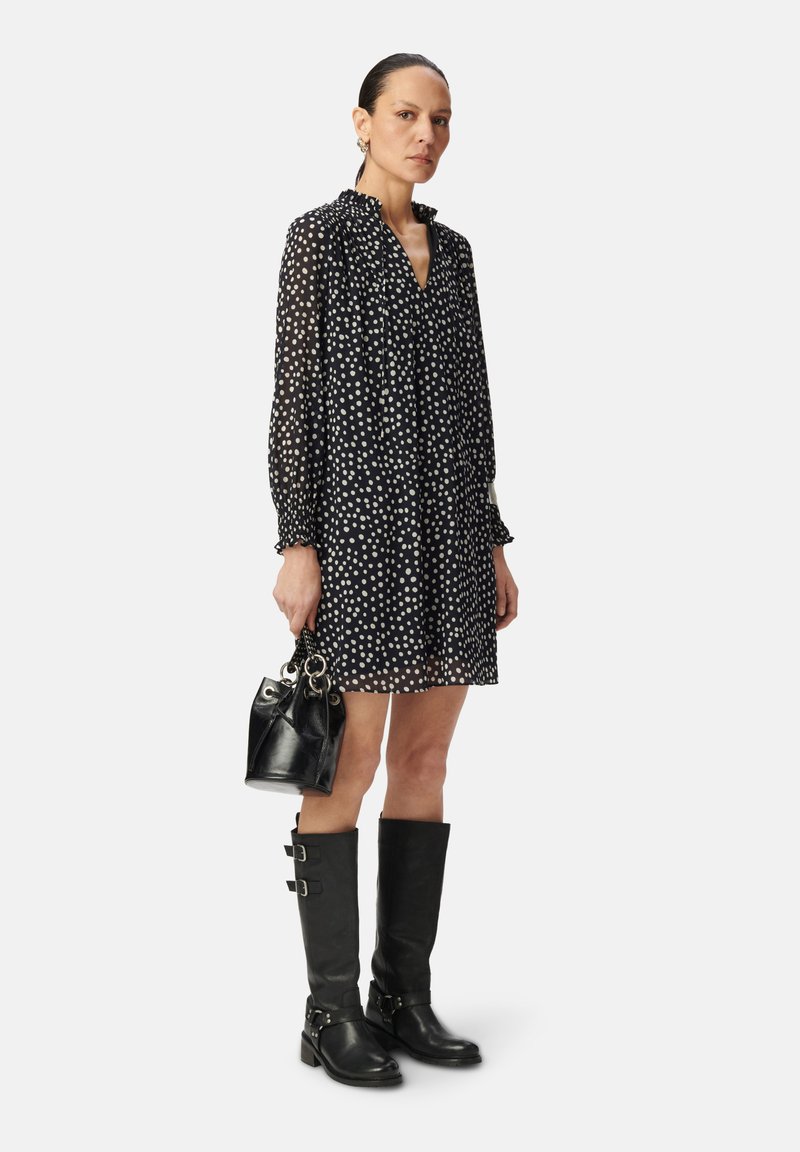 Vestido negro con lunares, con un escote con volantes, llevado con botas de cuero negras hasta la rodilla con hebillas y un pequeño bolso negro.