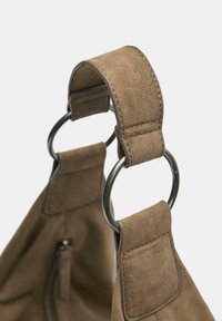 Brunt mockaskinnsrem för handväska med två metallringar som förbinder remmen med väskan, med en mjuk textur och tydlig sömdetalj.