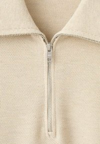 Beige trui met rits, gemaakt van een gebreide stof met structuur, voorzien van een zilveren rits en een opstaande kraag.
