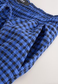 Shorts à carreaux bleus et noirs en tissu léger, avec une taille élastique et des poches latérales ; coupe décontractée avec une texture douce.