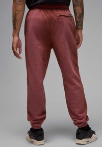 Bordeauxrote Jogginghose mit elastischem Bund, gerippten Bündchen und einer kleinen Gesäßtasche. Bietet eine weiche Textur und eine lockere Passform. Getragen mit schwarzen Sneakers.