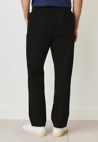 Black elastic-waist pants with a relaxed fit, featuring a subtle back pocket and smooth, lightweight material. Paired with white sneakers.