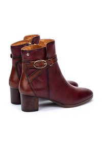 Bottines en cuir bordeaux avec un détail de sangle marron, fermeture éclair sur le côté et un talon en bois. Texture lisse avec un bout rond.