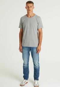 Grijze katoenen t-shirt met korte mouwen en een ronde hals, gecombineerd met lichtblauwe denim jeans en grijze sneakers met witte accenten.