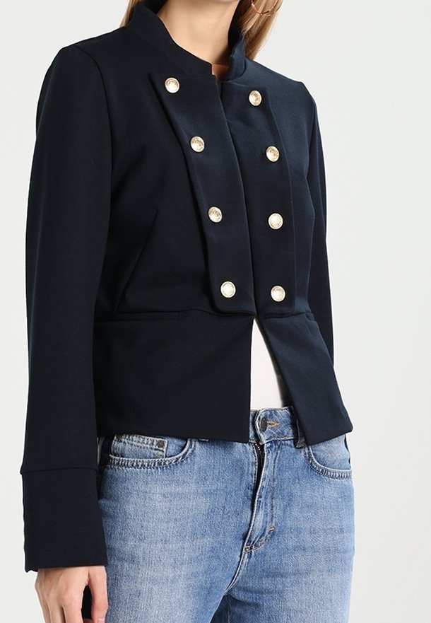 Marinblå strukturerad jacka med hög krage, försedda med sex stora pärlliknande knappar framtill och en kortad design.