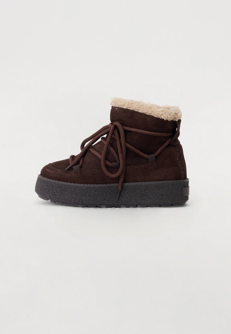 Bottines en suède marron avec un bord en fourrure synthétique, bout rond, semelle épaisse et texturée, et lacets marron. La vue de côté montre le détail du col rembourré.