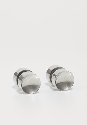 Sølvfargede metallmansjettknapper med en polert finish, som har sylinderform og en glatt tekstur, aksentuert av et sentralt mørkt bånd.
