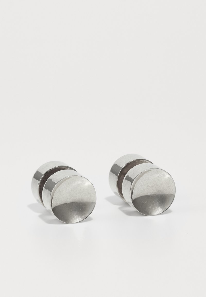 Boutons de manchette en métal argenté avec une finition polie, présentant une forme cylindrique et une texture lisse, accentués par une bande centrale foncée.
