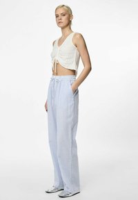 Witte crop top met strikdetail aan de voorkant, gecombineerd met lichtblauwe en witte gestreepte wijde broek. Model draagt zilveren schoenen.